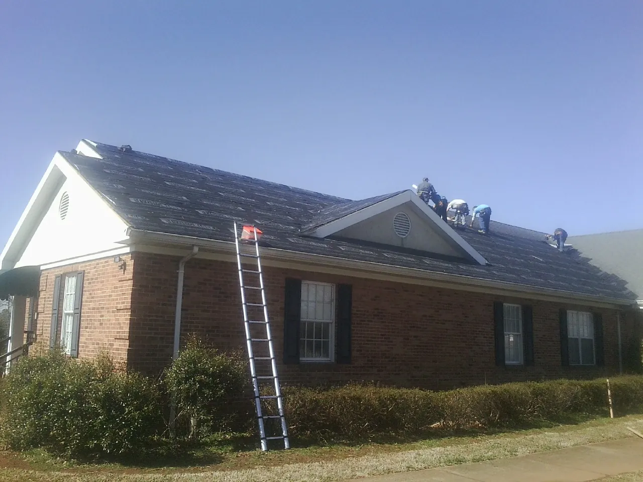 Crew tearing shingles off a brick ranch roof with a ladder set — Metal Roof Repair work by our crew in Glen Rock