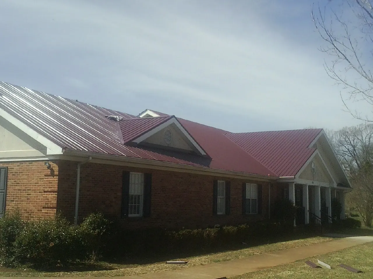 Red metal roof with gabled entries on a long brick building, from a Hail Damage Roof Repair job in Glen Rock