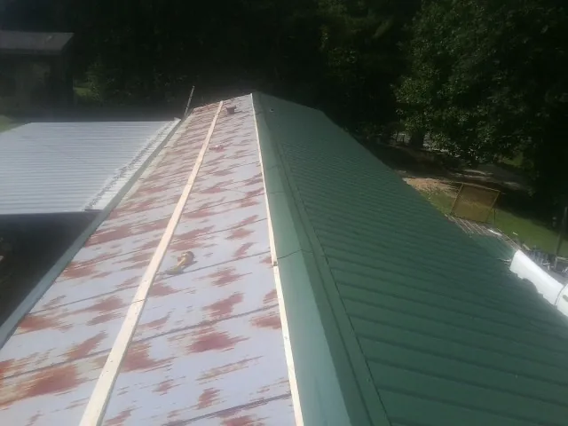 Old rusted panels beside newly installed green metal roofing — Wind Damage Roof Repair by Roofing Brothers in Glen Rock