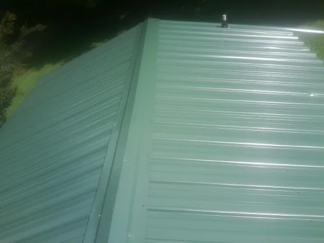 New green metal panels meeting at the ridge of a roof — Flat Roof Repair work by our crew in Glen Rock