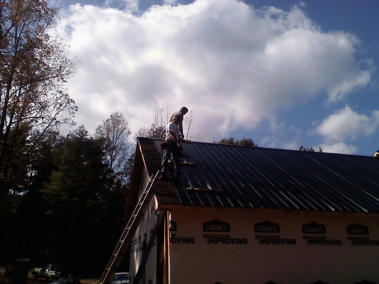 Roofer fastening dark metal panels high against a cloudy sky, from a Roof Inspection job in Glen Rock